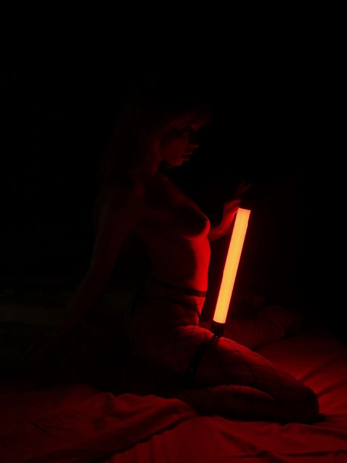 beautiful model kneeling in dim red light without bra holding a light torch