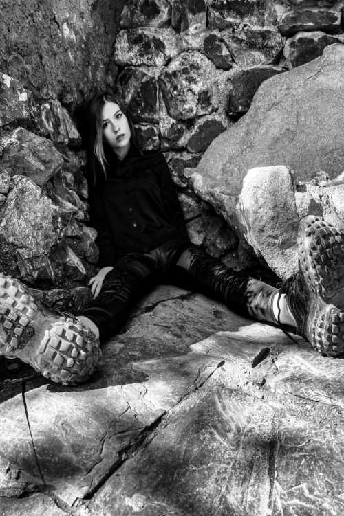 JessWoodstock sitting in front of a rock looking at the camera wearing hiking boots