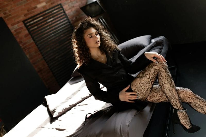MiaAxel sitting on a bed with her eyes closed, wearing an elegant outfit